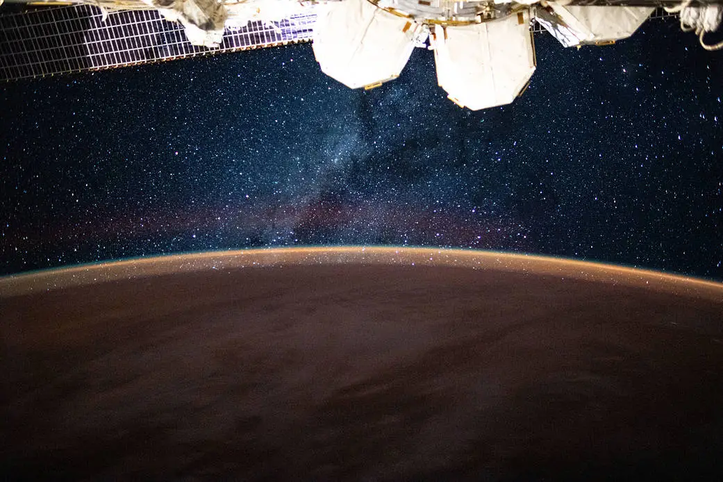 The Milky Way above Earth’s glowing horizon, photographed from the International Space Station, with station hardware along the top edge.